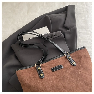 Detail der gesteppten braunen Tragetasche mit Metallnieten auf grauem Blazer