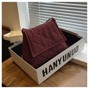 Detail of burgundy quilted crossbody bag with rhombic stitching texture in display box