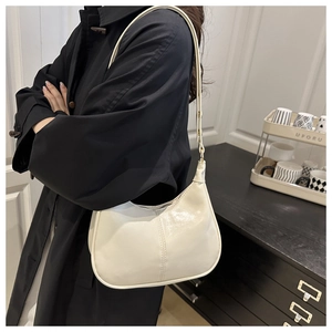 Detailed side view of a cream-colored leather dumpling bag worn with a black coat