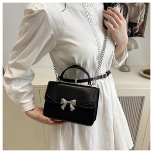 Detail of black crossbody bag with silver bow accent and chain strap worn by a model
