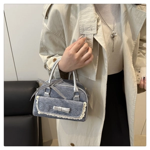 Detail of denim handbag with lace pockets, silver bow, and checkered ribbon on model