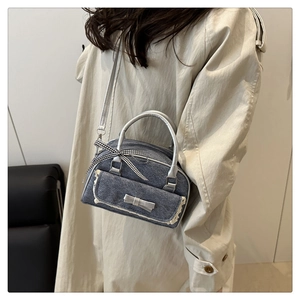 Detail of grey denim crossbody bag with white lace trim and silver bow charm accent