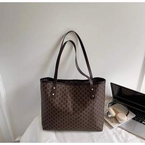 Detail of brown tote bag with M-letter texture, gold rivets and premium faux leather straps