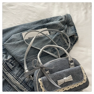 Detail of denim handbag with white lace trim and plaid bow accents on fabric background