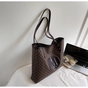 Detail of the embossed brown leather M logo and repeat pattern on a tote bag surface
