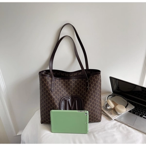 Detail of large brown tote bag with M-pattern print and laptop for commuting lifestyle
