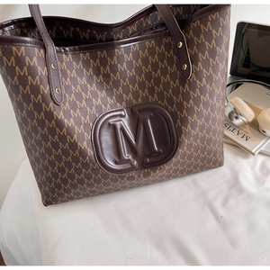 Macro detail of large embossed M logo on a brown monogram tote bag with leather texture