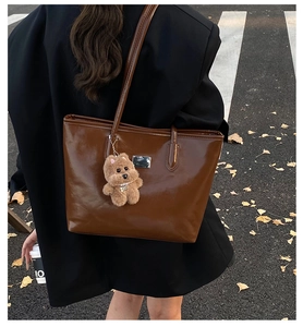Detail of a large brown tote bag with a cute teddy bear charm on a female model