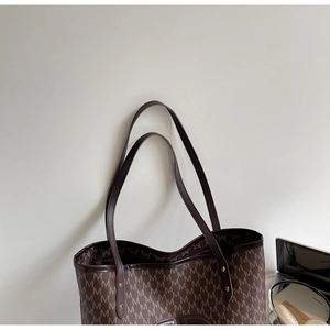 Detail of a large tote bag featuring brown leather trim and M-letter print on canvas