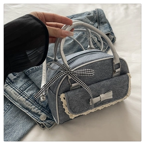 Detailed view of denim handbag featuring white lace trim and silver bow accents