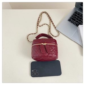 Top view of deep burgundy quilted mini box bag with gold chain and handle on a desk
