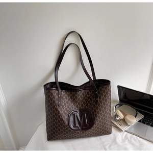 Macro detail of brown tote bag with embossed M logo and monogram pattern on faux leather