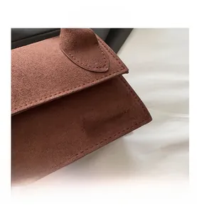 Close-up of brown suede crossbody bag featuring a golden metal logo and textured finish