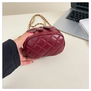 Detailed shot of a burgundy quilted box bag with a golden chain strap in an office setting
