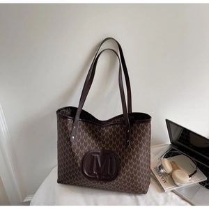 Detail of large tote bag featuring M-pattern monogram and embossed leather logo patch