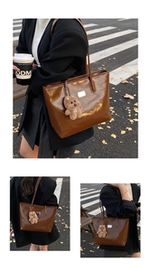 Detail of vintage brown patent leather tote bag with metallic plaque and plush bear charm