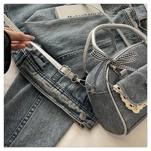 Detail of denim Boston bag featuring lace edges, checkered bow, and leather straps