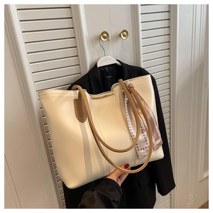 Detail of a cream tote bag with brown handles and a decorative fashion scarf detail