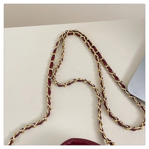Detail of burgundy quilted bag with gold metal and leather woven chain shoulder strap