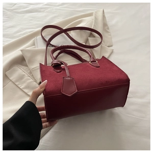 Détail du sac bandoulière bordeaux avec coutures en daim et pendentif carré élégant