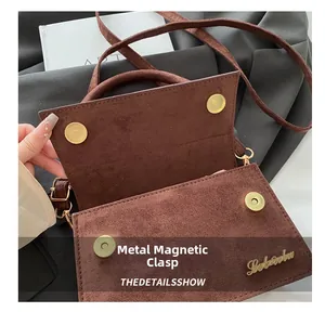 Detail shot of the double magnetic gold hardware closure on a brown suede crossbody bag