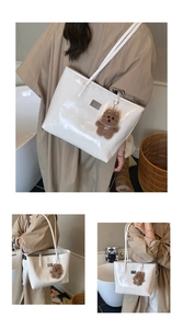 Close-up of white glossy patent leather tote bag featuring a cute brown plush bear charm
