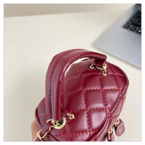 Detail of burgundy quilted leather mini box bag with gold metal hardware and top handle