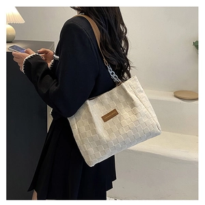 Close-up of a cream woven tote bag featuring a leather logo patch and silver chain strap