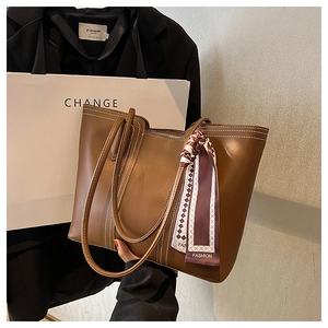 Detail of a brown leather tote bag with white contrast stitching and a silk scarf accent