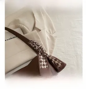Detail of dark brown leather shoulder bag with chic checkered ribbon bow decoration