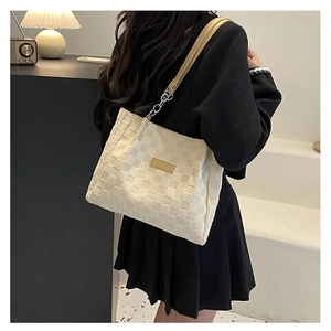 Detail of beige checkered woven tote bag with chain strap and leather patch on model