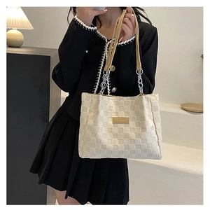 Close-up of cream woven tote bag featuring brown leather straps and metallic chain detail