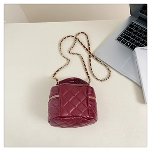 Detail view of burgundy quilted crossbody bag with gold chain and top handle on a desk