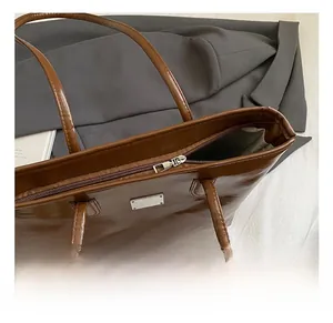 Close-up of brown leather tote showing silver metal hardware and zipper detail