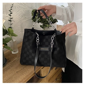Detail of black checkered tote bag featuring a silver chain handle and magnetic closure