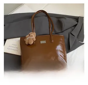 Detail of a brown glossy tote bag with a cute plush bear charm and silver metal logo plate