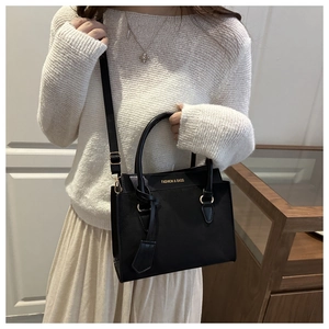 Detail of elegant black matte leather handbag with gold logo and adjustable shoulder strap
