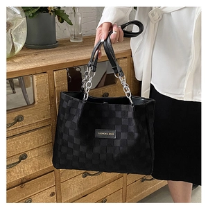 Macro detail of black checkered tote bag with silver chain strap and logo patch