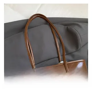 Detail of dark brown patent leather tote with a plush bear charm and sleek handles