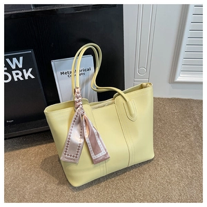 Close-up of a pale yellow tote bag with a decorative fashion silk scarf on the handle