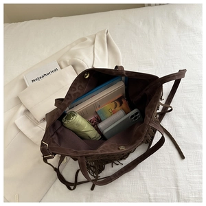Detail view of brown tassel tote bag showing spacious interior with books and daily essentials