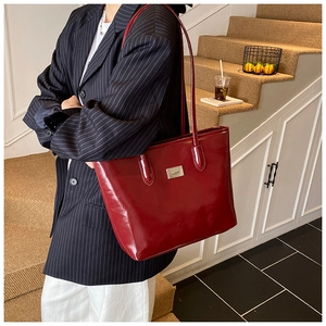 Détail du cabas en cuir verni rouge foncé avec logo crocodile sur un blazer rayé