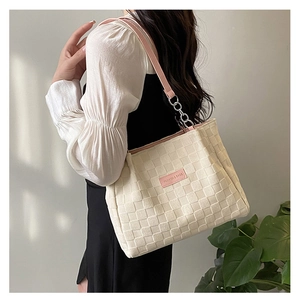 Close-up of cream quilted tote bag featuring a pink brand label and metal chain strap