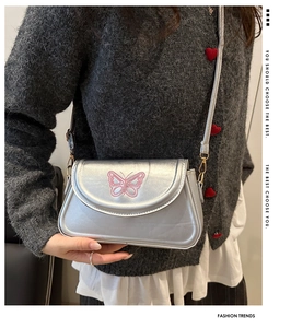 Détail d'un sac à bandoulière argenté avec broderie papillon rose et fini métallisé
