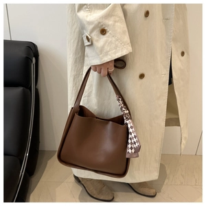 Detail of dark brown leather tote bag featuring a checkered silk scarf on handle