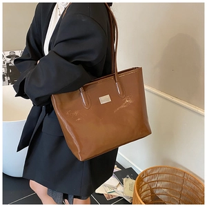 Brown glossy patent leather tote bag detail with metallic plate and thin shoulder straps