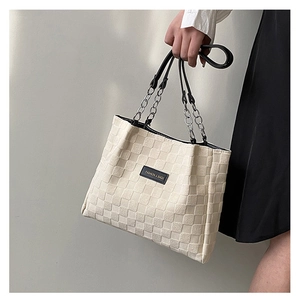 Detail of cream tote bag with woven texture, black handles and silver chain links