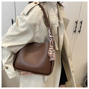 Brown leather tote bag detail with checkered scarf accent worn over a beige trench coat