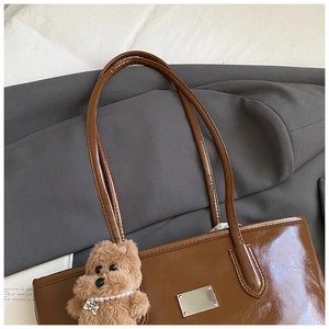 Détail du sac cabas en cuir marron brillant avec plaque métal et breloque chien peluche