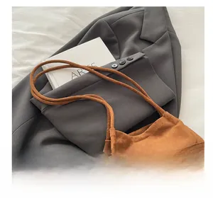 Détail d'un sac seau en daim marron à franges posé sur un blazer de bureau gris